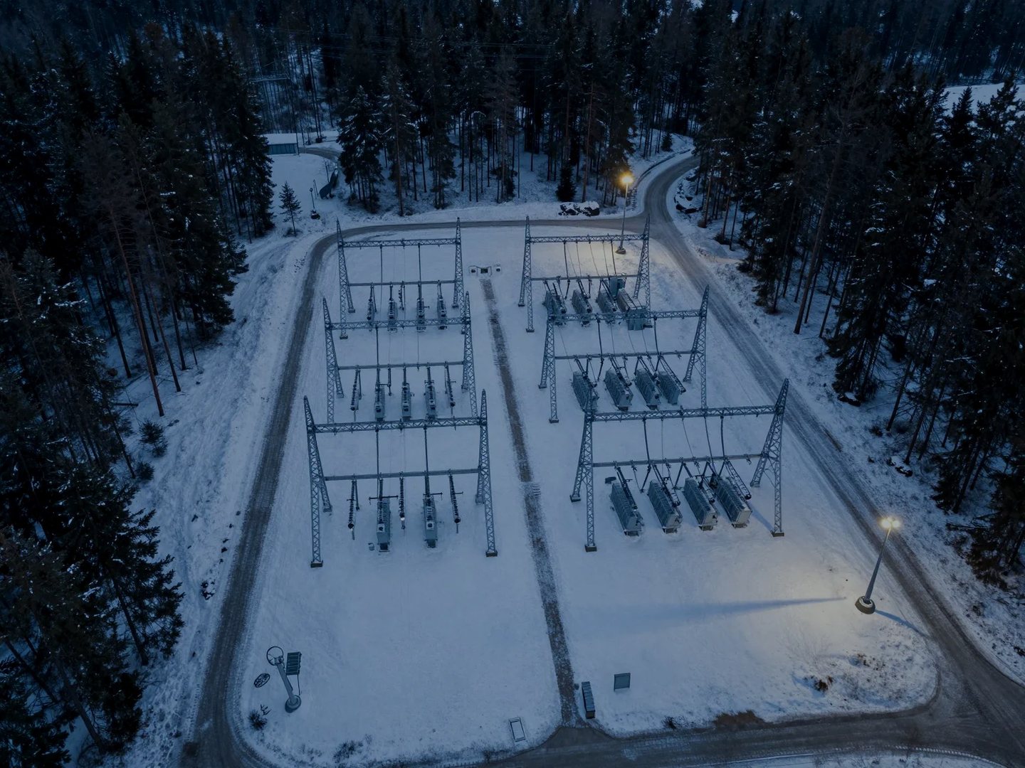 Aerial view of a substation in a snowy forest clearing at dusk
